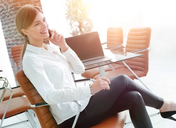 young female assistant talking on phone sitting near the desktop.