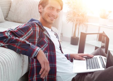 modern oturma odasında otururken dizüstü bilgisayar ile büyüleyici genç adam