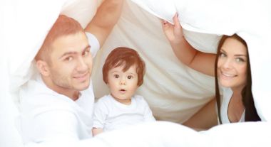 mutlu bir aile kameraya bakarken bir yorgan altında poz