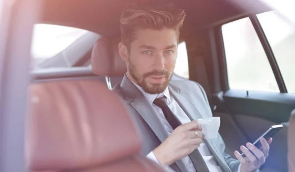 Uomo d'affari che beve caffè in auto con il telefono in mano — Foto Stock