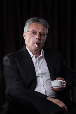 bir sigara ve bir fincan kahve tutan işadamı