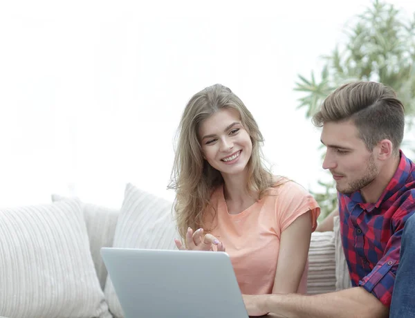 Jong paar is met behulp van een laptop en glimlachend zittend op de Bank thuis — Stockfoto