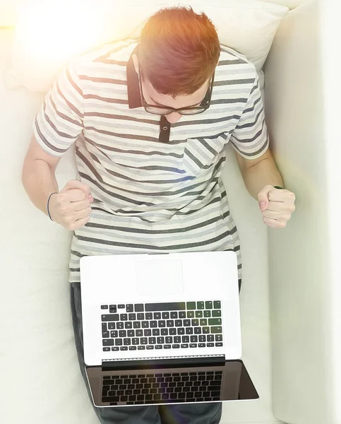 Feliz hombre moderno mira el portátil sentado en el sofá . —  Fotos de Stock