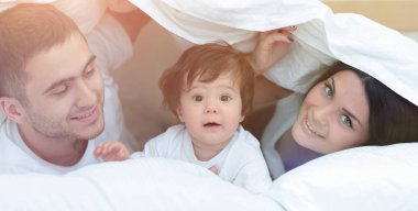 mutlu bir aile kameraya bakarken bir yorgan altında poz
