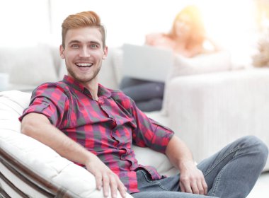 Bulanık arka planda büyük bir sandalyede oturan mutlu genç adam.