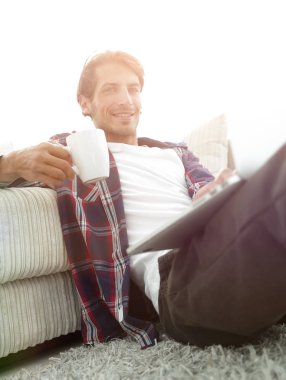 dizüstü bilgisayar yakınındaki inci katta oturan bir fincan holding ile genç adam