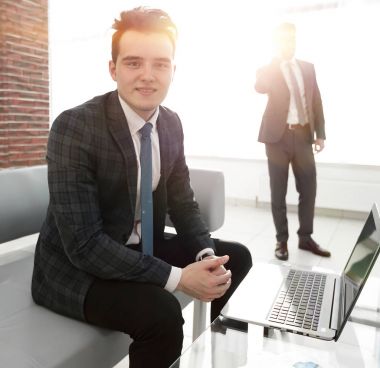 Genç işadamı ofiste dizüstü bilgisayarla çalışıyor.