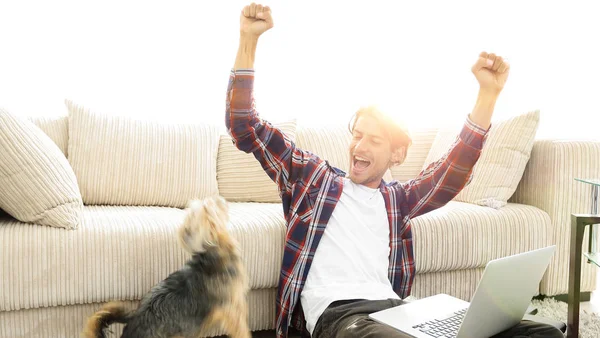 Jovem feliz exulta com seu cão sentado na sala de estar — Fotografia de Stock