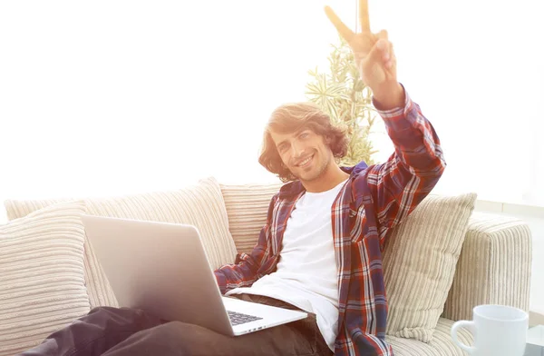 Mutlu adam kanepede oturan ve elini bir galibiyet gösterilen dizüstü bilgisayar ile — Stok fotoğraf