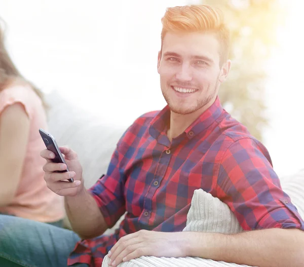 Chico moderno con un teléfono inteligente y sus amigos sentados en el couc — Foto de Stock