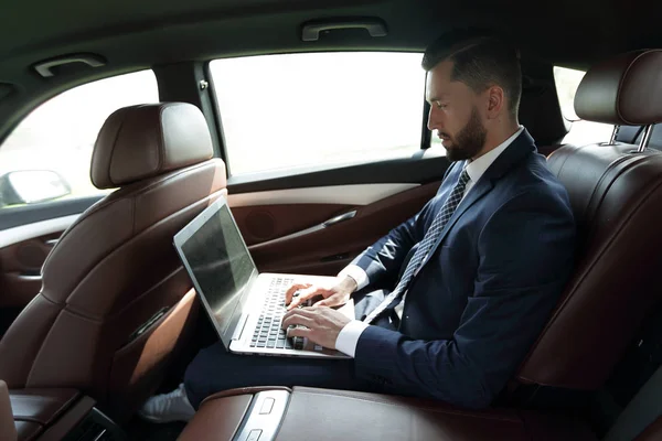 Uomo d'affari che utilizza un computer portatile nel sedile posteriore di una macchina — Foto Stock