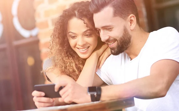 Feliz pareja amorosa usando un teléfono inteligente sentado en la terraza —  Fotos de Stock