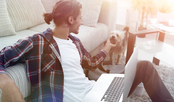 Stijlvolle jongeman streelde zijn huisdier en bezig met laptop — Stockfoto