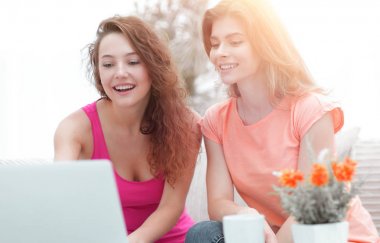 iki öğrenci kız kanepede otururken dizüstü bilgisayar ekranına bakarak.