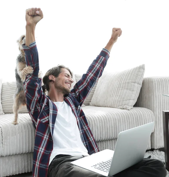 Glücklicher Kerl jubelt mit seinem Hund, der neben dem Sofa im Wohnzimmer sitzt. — Stockfoto