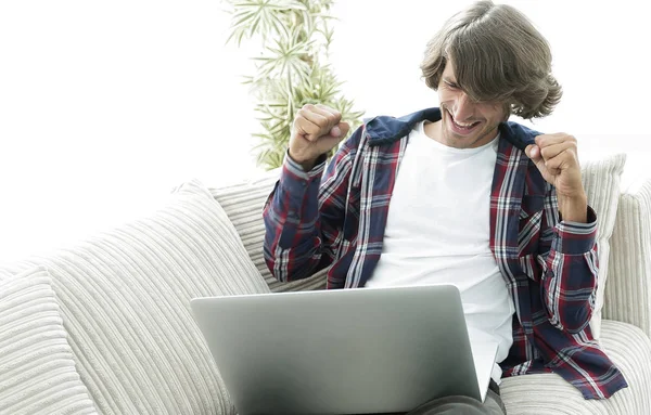 Χαρούμενος ο τύπος με το laptop που κάθεται στον καναπέ. έννοια της επιτυχίας — Φωτογραφία Αρχείου