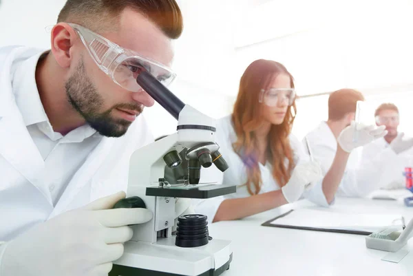 Manliga laboratorietekniker tittar på prover i mikroskopet — Stockfoto