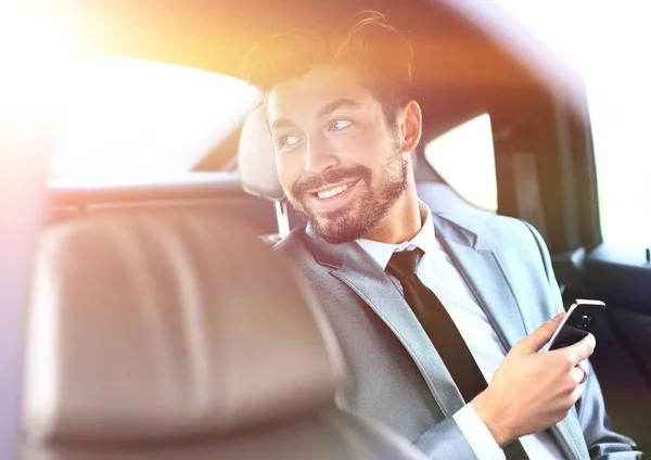Unsmiling businessman sitting in the back seat in his car — Stock Photo, Image