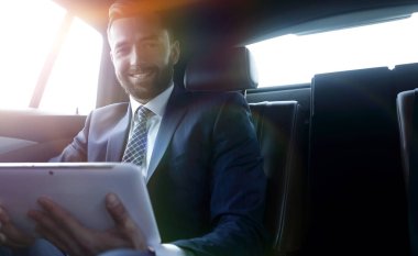 bir arabanın arka koltuğunda çalışma ve bir tablet kullanarak iş adamı