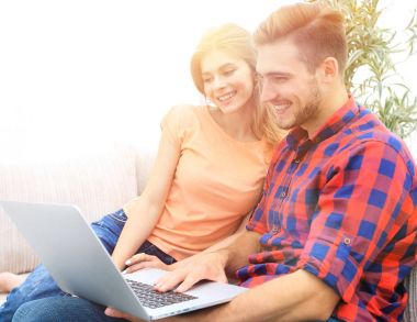 Genç çift kanepede oturan dizüstü bilgisayar ile gülümseyen