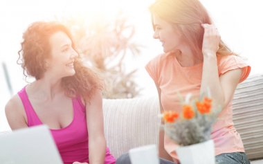 İki genç kadın kahve masasında konuşuyor ve oturuyor.