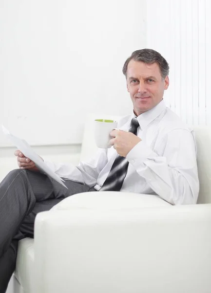 Jistý podnikatel pití čaje a čtení dokumentu, sedí v křesle v hotelovém pokoji — Stock fotografie