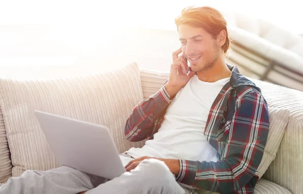 Joven serio con el ordenador portátil hablando por teléfono móvil —  Fotos de Stock