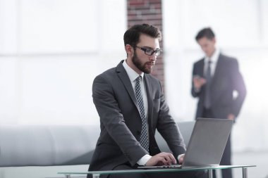 Yakışıklı iş adamı ofiste dizüstü bilgisayarla çalışıyor.