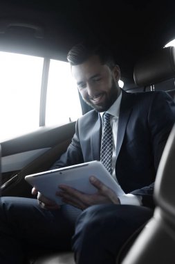 bir arabanın arka koltuğunda oturan bir dijital tablet ile işadamı