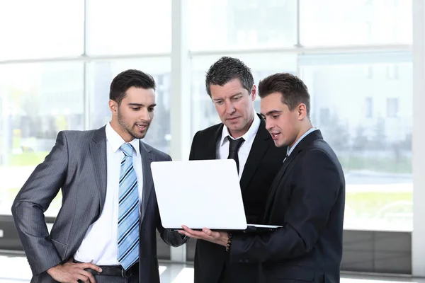 Коллеги по бизнесу смотрят на ноутбук, стоящий в холле офиса . — стоковое фото