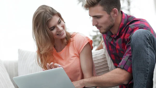 Giovane coppia sta utilizzando un computer portatile e sorridente mentre seduto sul divano a casa — Foto Stock