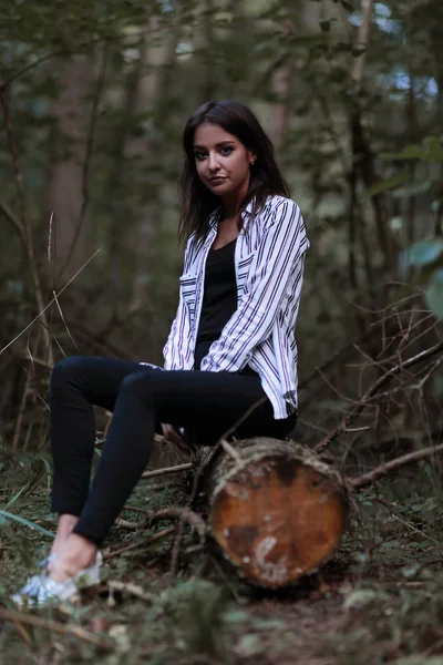 Mujer joven sentada en un tronco en el bosque . — Foto de Stock
