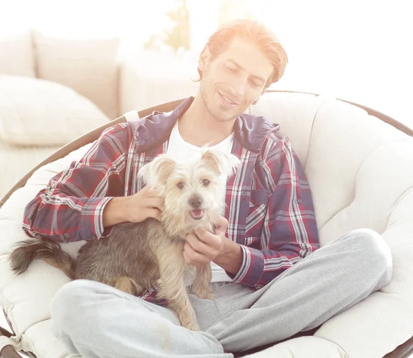Cara bonito com um cão sentado em uma poltrona grande . — Fotografia de Stock