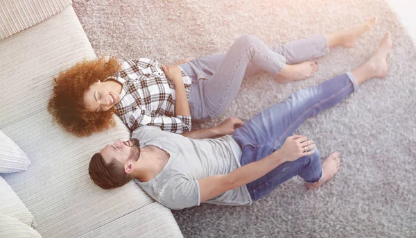 Sonriente pareja acostada en una alfombra en un nuevo apartamento — Foto de Stock