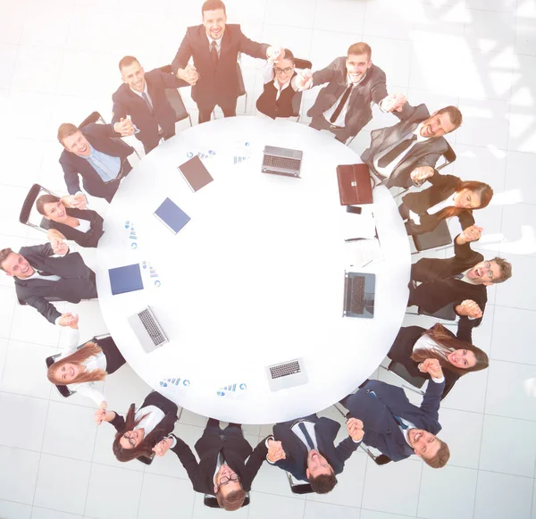 Diretor e equipe de negócios sentados na mesa redonda e segurando as mãos uns dos outros . — Fotografia de Stock