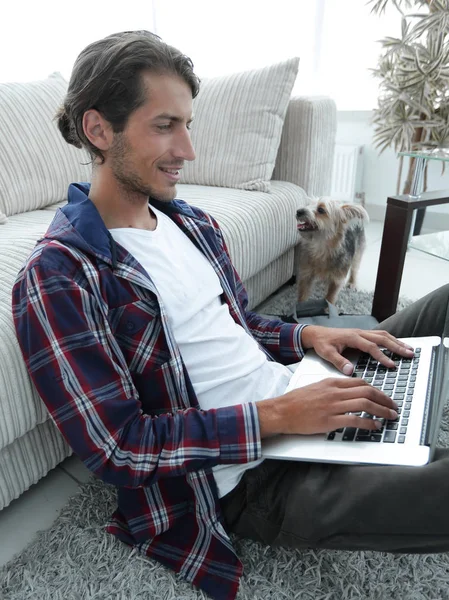 Ragazzo moderno con un computer portatile seduto sul pavimento vicino al divano — Foto Stock