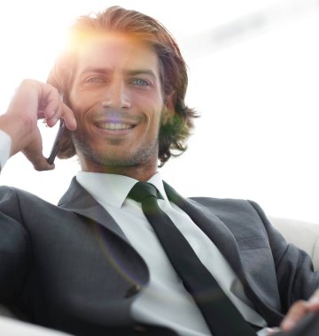 iş adamı rahat bir sandalyede otururken Smartphone'da konuşuyor.