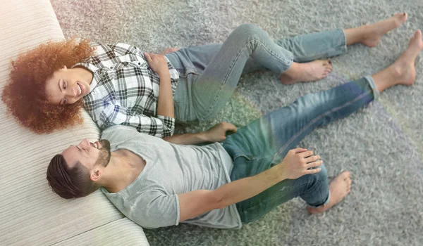 Sonriente pareja acostada en una alfombra en un nuevo apartamento — Foto de Stock