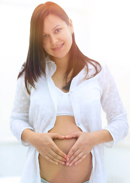 beautiful pregnant woman holding hands in heart shape on her belly.