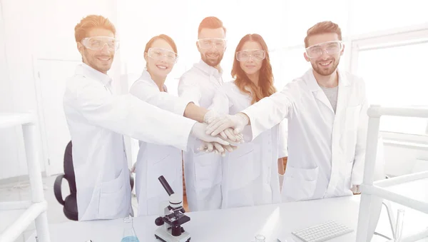 Equipe bem sucedida de jovens cientistas com as mãos apertadas juntas . — Fotografia de Stock