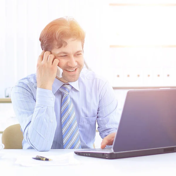 Bell'uomo d'affari seduto alla scrivania e che parla al cellulare — Foto Stock