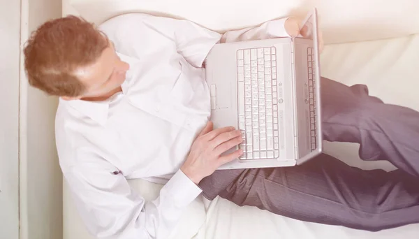View from the top.man working on laptop lying on a sofa. — Stock Photo, Image