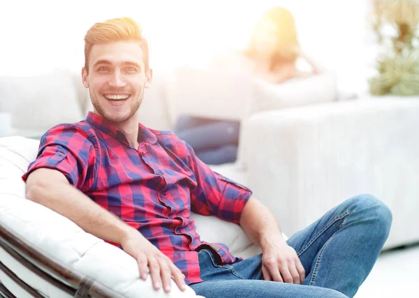 Bulanık arka planda büyük bir sandalyede oturan mutlu genç adam.