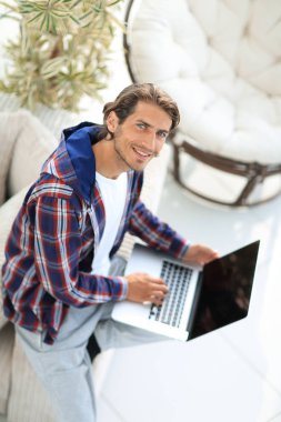 dizüstü bilgisayarda çalışan ve kameraya bakarak bir genç adam. Yukarıdan görüntülemek