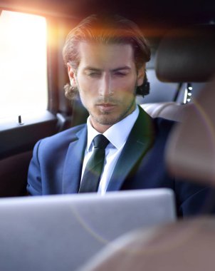 Adam arabada otururken dizüstü bilgisayarla çalışıyor.