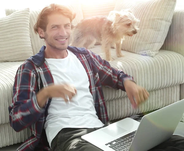 Felice giovane uomo esulta con il suo cane seduto in salotto — Foto Stock