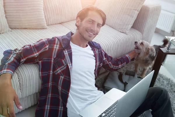 Cara de sucesso acariciando seu animal de estimação sentado no chão perto do assim — Fotografia de Stock