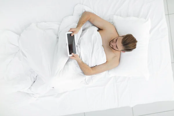 Homem sorrindo usando tablet digital deitado na cama — Fotografia de Stock