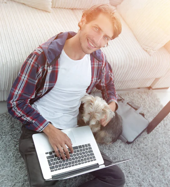 Jóképű srác laptop átölelve a kutyáját, és közel a kanapén ül — Stock Fotó