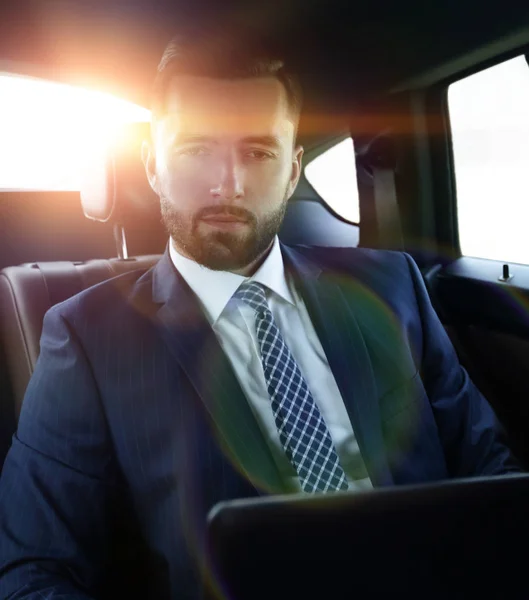 Businessman with laptop sitting in a comfortable car — Stock Photo, Image